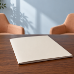 Blank cream booklet on a dark wooden table with two empty apricot chairs and a pale-blue wall